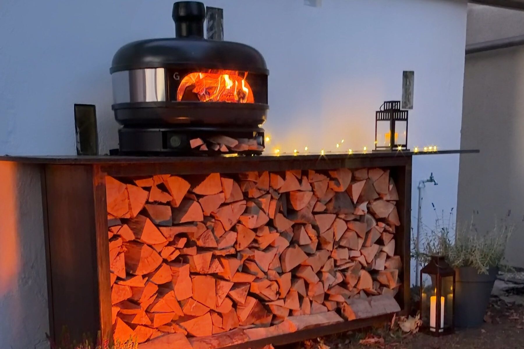 Kaminholzregal aus Cortenstahl mit Granitplatte und Pizzaofen am Abend