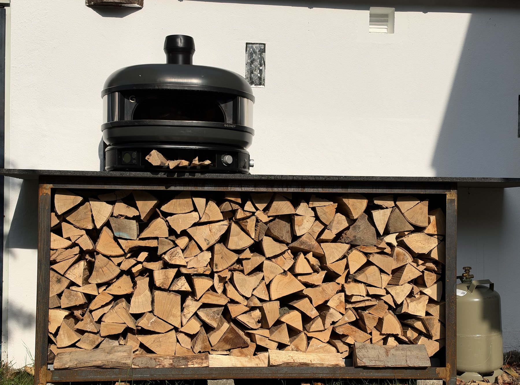 Kaminholzregal aus Cortenstahl mit Granitplatte, auf Betonplatten an der Hauswand